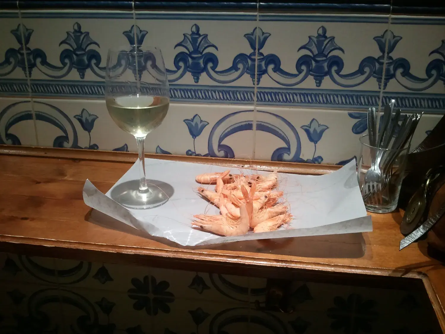 Tapa de crevettes blanches accompagnée d’un verre de vin blanc sur un comptoir carrelé