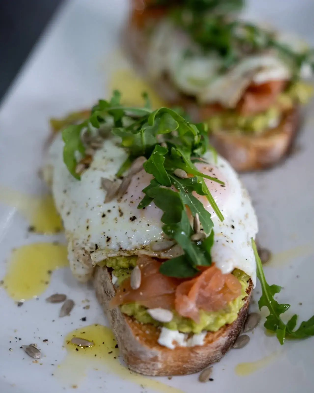 Tostada garnie d’avocat, saumon fumé, œuf au plat, roquette et graines de tournesol chez Hola Patatas