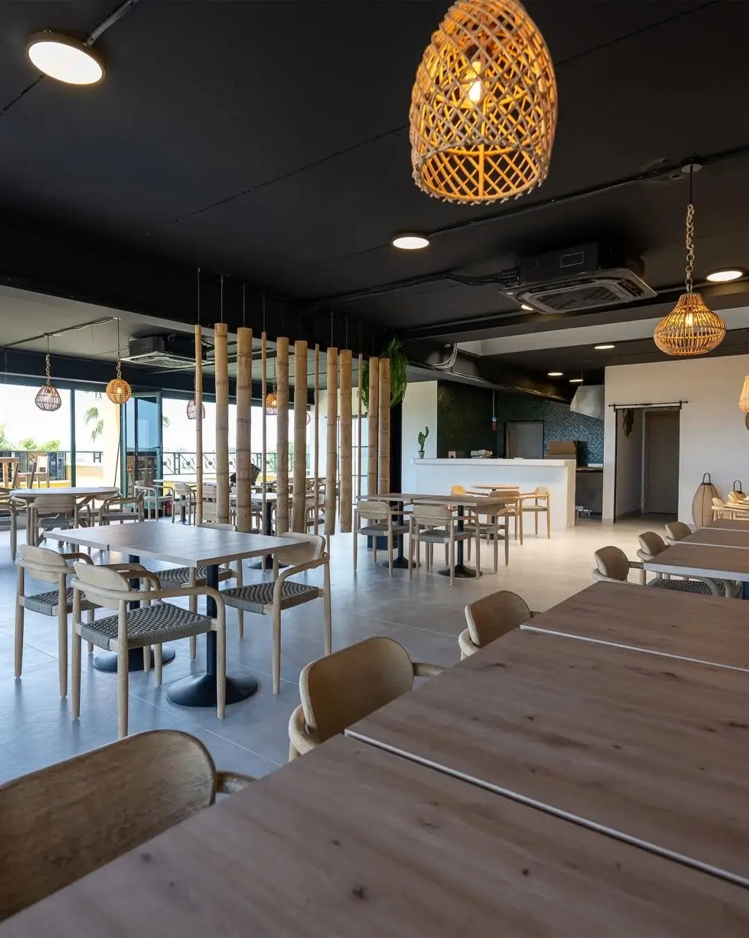 Salle lumineuse de Hola Patatas avec tables en bois, chaises tressées, suspensions en rotin et séparation en bambou