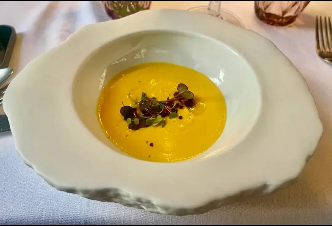 Velouté de potiron offert au Restaurante Luka, servi dans une assiette creuse blanche aux bords irréguliers et décoré de jeunes pousses